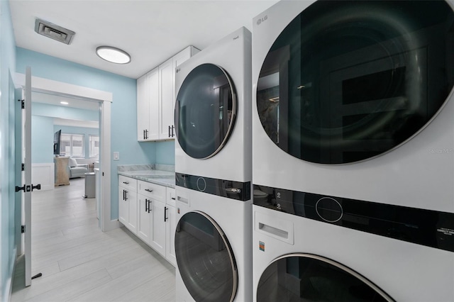 clothes washing area with cabinets, stacked washer / dryer, light wood-type flooring, and washing machine and dryer