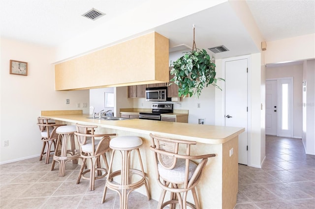 kitchen featuring a breakfast bar, sink, light tile patterned floors, appliances with stainless steel finishes, and kitchen peninsula