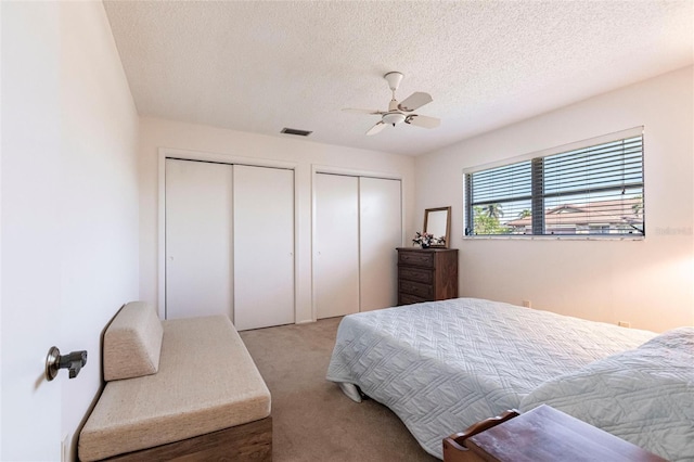 carpeted bedroom with ceiling fan, a textured ceiling, and two closets