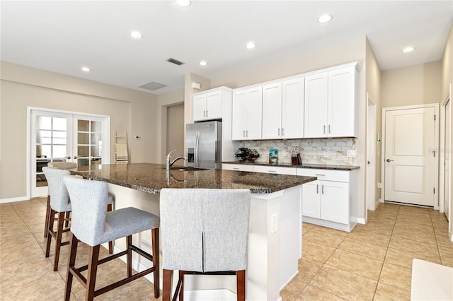 kitchen featuring stainless steel fridge with ice dispenser, white cabinets, and a center island with sink