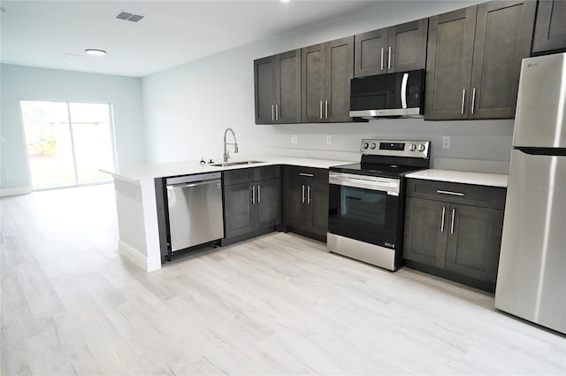 kitchen featuring sink, light hardwood / wood-style floors, kitchen peninsula, stainless steel appliances, and dark brown cabinets