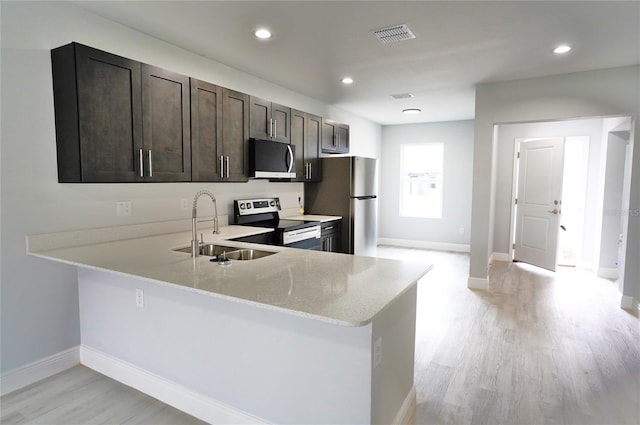 kitchen featuring sink, light stone counters, kitchen peninsula, stainless steel appliances, and dark brown cabinets