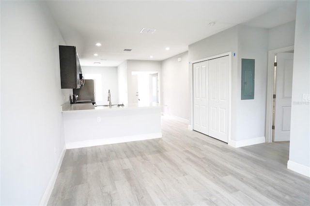 unfurnished living room featuring electric panel, sink, and light wood-type flooring