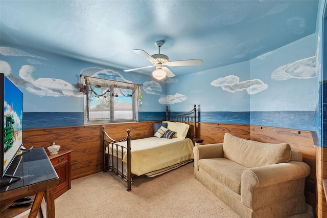 bedroom with light carpet, wooden walls, and ceiling fan