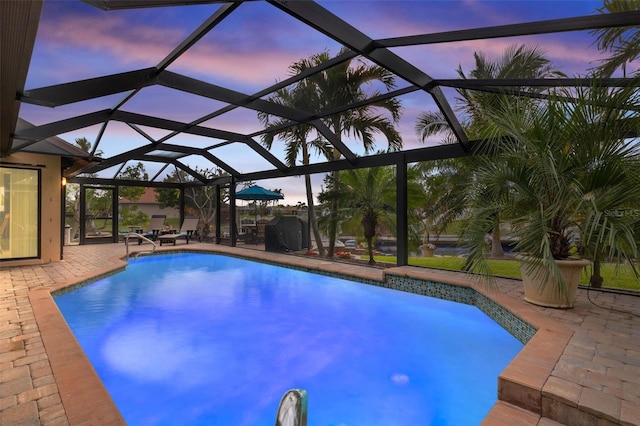 pool at dusk featuring glass enclosure and a patio area