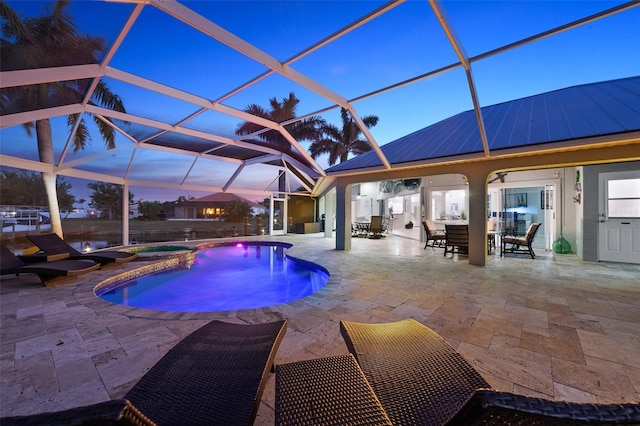 pool at dusk with a patio area, an in ground hot tub, and glass enclosure