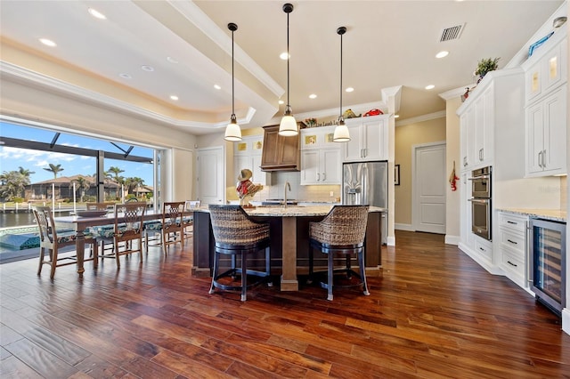 kitchen featuring white cabinetry, stainless steel appliances, wine cooler, a center island with sink, and decorative light fixtures