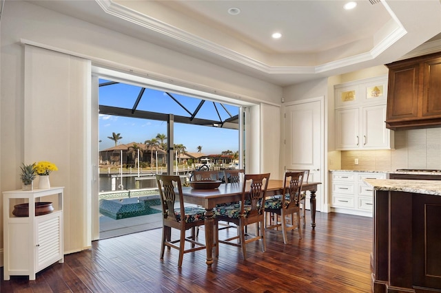 dining area featuring crown molding, a tray ceiling, dark wood-type flooring, and a water view