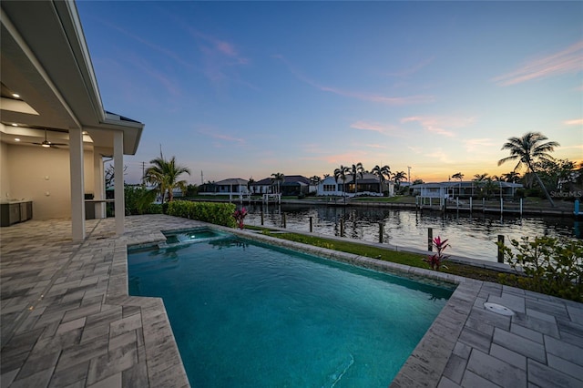 pool at dusk with a patio, a water view, an in ground hot tub, and ceiling fan