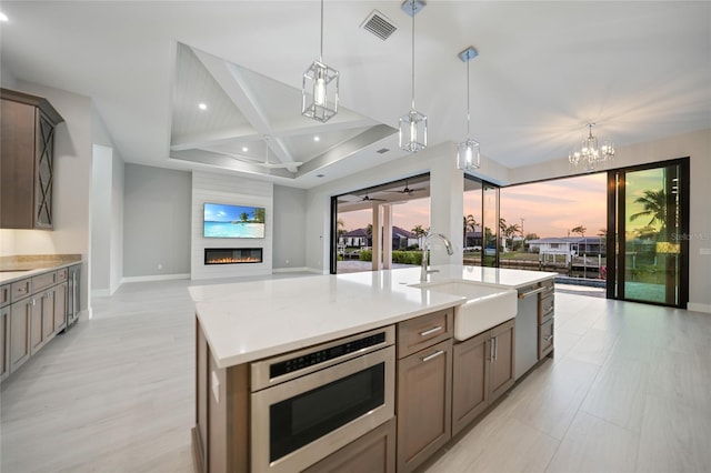 kitchen featuring a kitchen island with sink, sink, pendant lighting, and stainless steel microwave