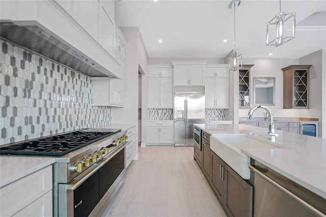 kitchen featuring pendant lighting, sink, white cabinets, built in appliances, and light stone countertops