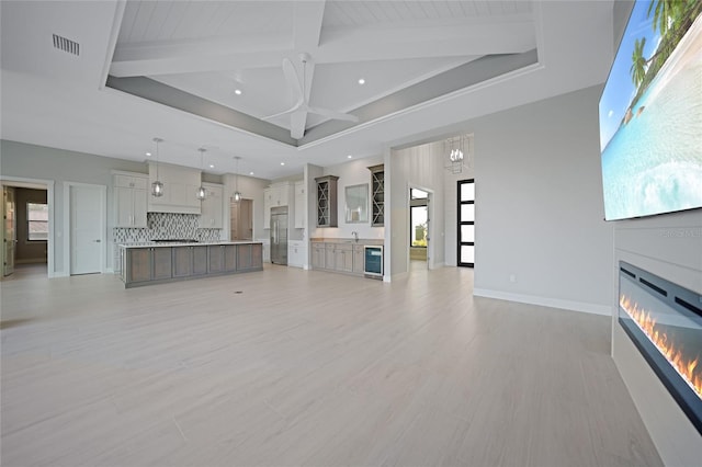 unfurnished living room with beam ceiling, a chandelier, light wood-type flooring, a towering ceiling, and beverage cooler