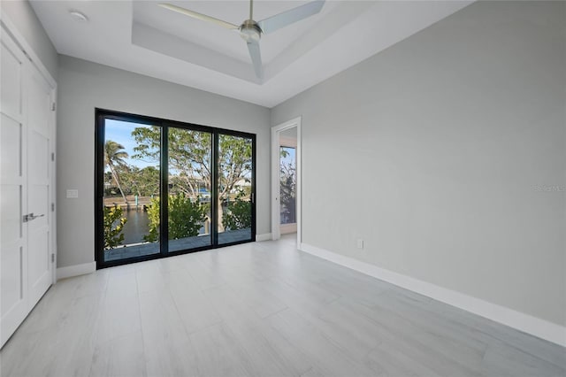 empty room featuring a water view, ceiling fan, and a raised ceiling