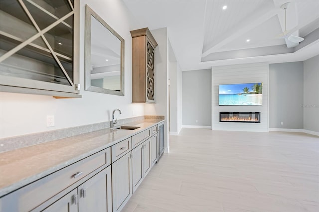 bar with light stone counters, sink, and a raised ceiling