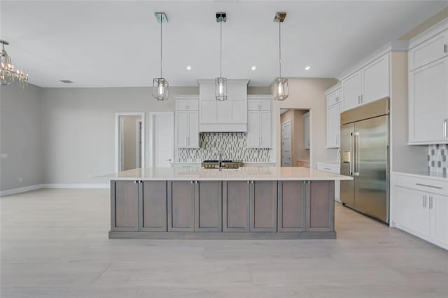 kitchen with pendant lighting, white cabinetry, a spacious island, tasteful backsplash, and built in fridge