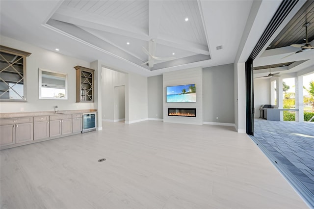 living room with a fireplace, beamed ceiling, beverage cooler, ceiling fan, and a raised ceiling