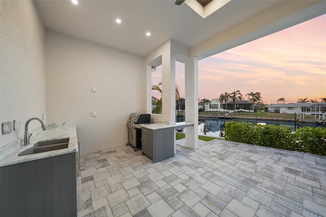 patio terrace at dusk with exterior kitchen, a water view, sink, and grilling area