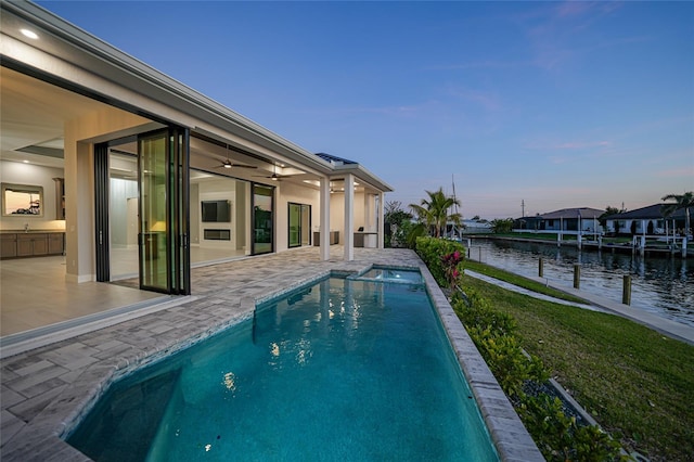 pool at dusk with a patio, a water view, sink, and ceiling fan