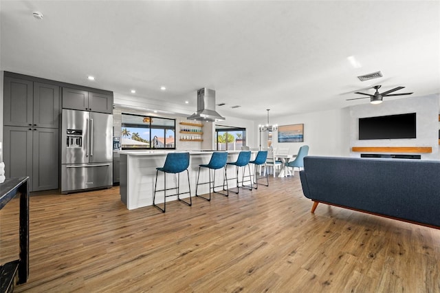 kitchen with gray cabinets, a breakfast bar area, island range hood, high quality fridge, and a kitchen island