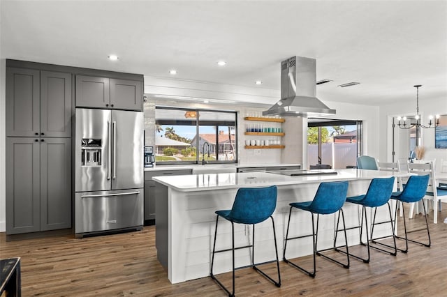 kitchen with a breakfast bar area, island range hood, high quality fridge, gray cabinets, and a kitchen island with sink