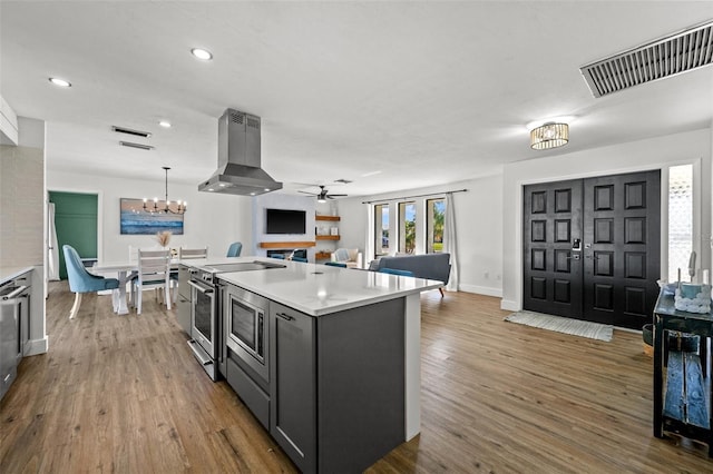 kitchen featuring stainless steel electric stove, pendant lighting, wood-type flooring, island exhaust hood, and a kitchen island with sink