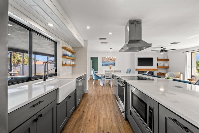 kitchen featuring sink, stainless steel appliances, light stone counters, island range hood, and decorative light fixtures