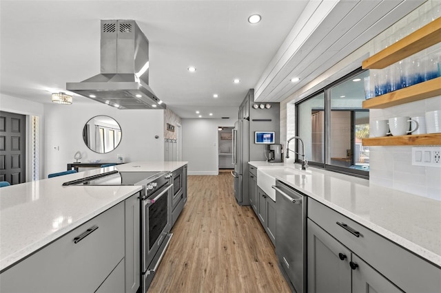 kitchen with gray cabinets, island range hood, sink, high end appliances, and light stone counters