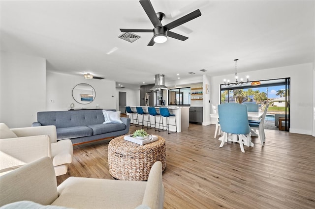 living room with ceiling fan with notable chandelier and light hardwood / wood-style floors