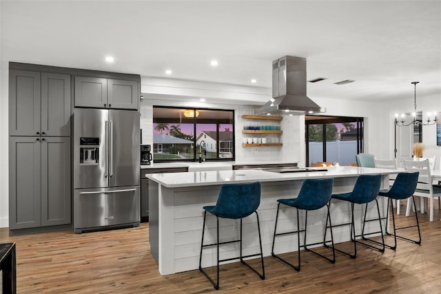 kitchen with a spacious island, a kitchen bar, high end fridge, gray cabinets, and island exhaust hood