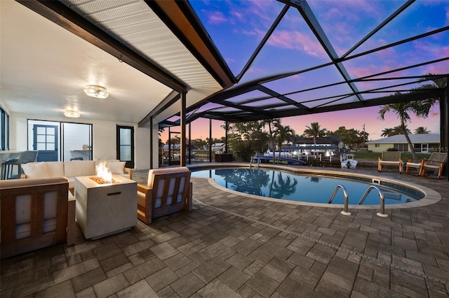 pool at dusk featuring a lanai, a patio area, and an outdoor living space with a fire pit