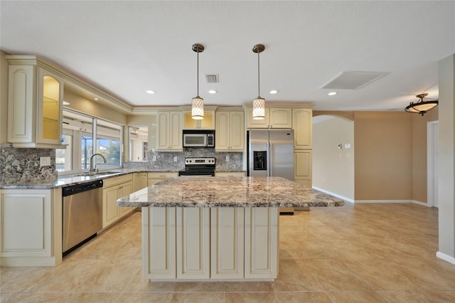 kitchen featuring sink, stainless steel appliances, a center island, light stone countertops, and decorative backsplash