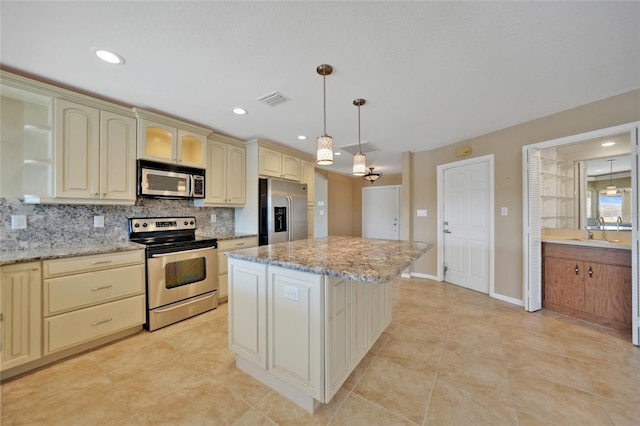 kitchen featuring backsplash, hanging light fixtures, stainless steel appliances, light stone countertops, and a kitchen island