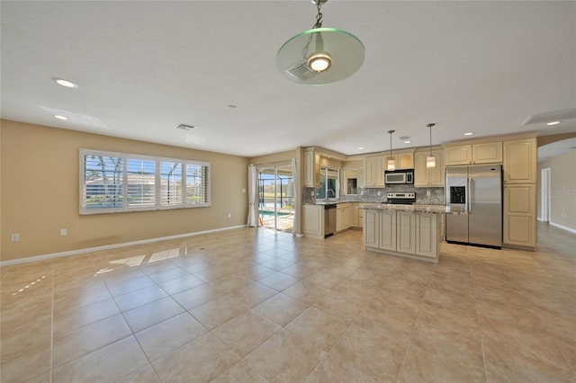 kitchen with light stone counters, hanging light fixtures, appliances with stainless steel finishes, a kitchen island, and backsplash