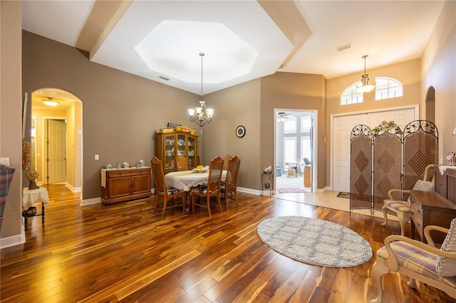 dining space featuring dark wood-type flooring, a raised ceiling, and an inviting chandelier