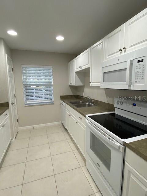 kitchen with white cabinetry, sink, light tile patterned floors, and white appliances