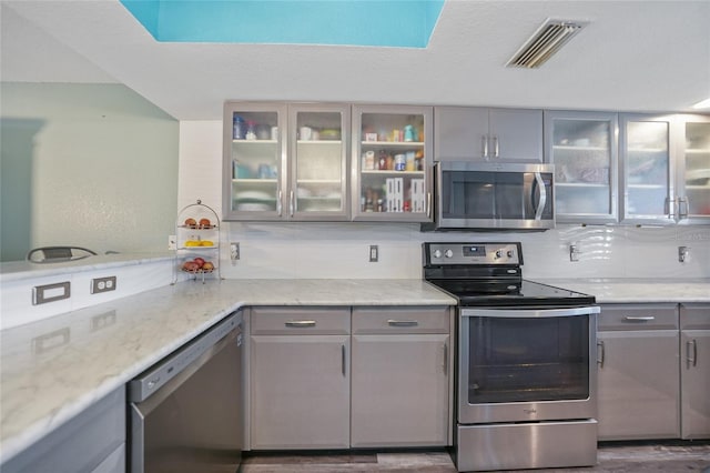 kitchen featuring stainless steel appliances, dark hardwood / wood-style floors, light stone countertops, and gray cabinetry