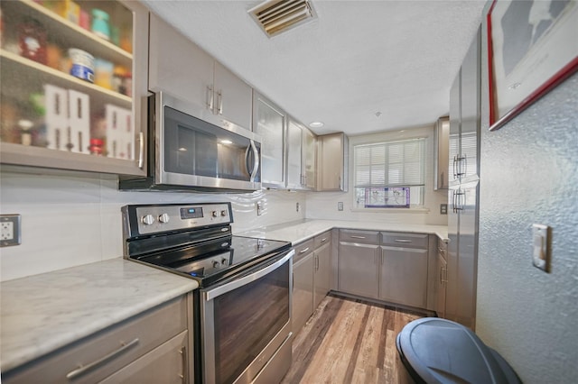 kitchen with gray cabinets, pendant lighting, light stone counters, stainless steel appliances, and light hardwood / wood-style flooring