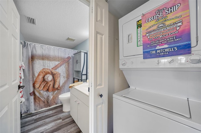 laundry area with dark wood-type flooring, stacked washer and clothes dryer, and a textured ceiling