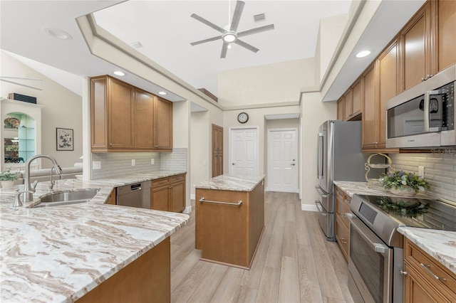 kitchen featuring sink, appliances with stainless steel finishes, kitchen peninsula, a kitchen island, and light stone countertops