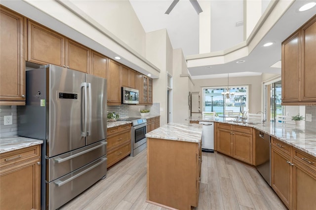 kitchen featuring a kitchen island, appliances with stainless steel finishes, sink, kitchen peninsula, and light stone countertops