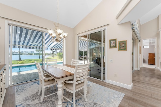 dining room featuring a water view, lofted ceiling, a chandelier, and light hardwood / wood-style floors