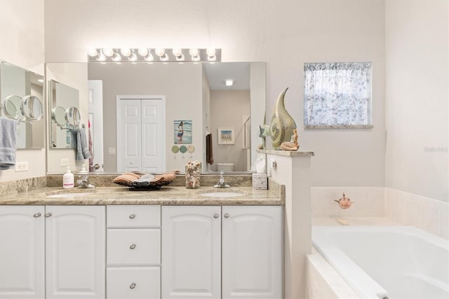 bathroom with vanity, tiled tub, and toilet