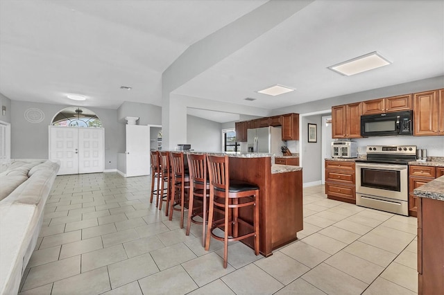 kitchen featuring a kitchen bar, open floor plan, appliances with stainless steel finishes, light tile patterned floors, and baseboards