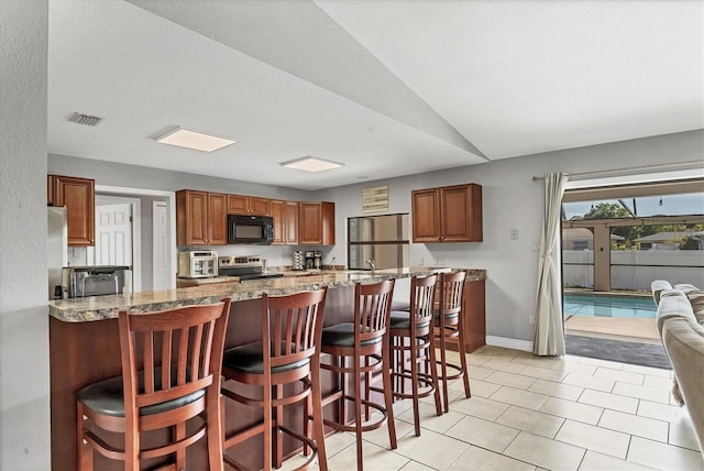 kitchen with light stone counters, visible vents, stainless steel appliances, a kitchen bar, and brown cabinets