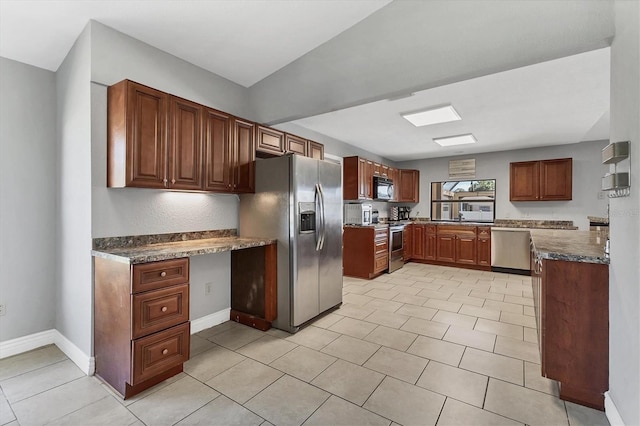 kitchen featuring dark countertops, baseboards, built in desk, stainless steel appliances, and a sink