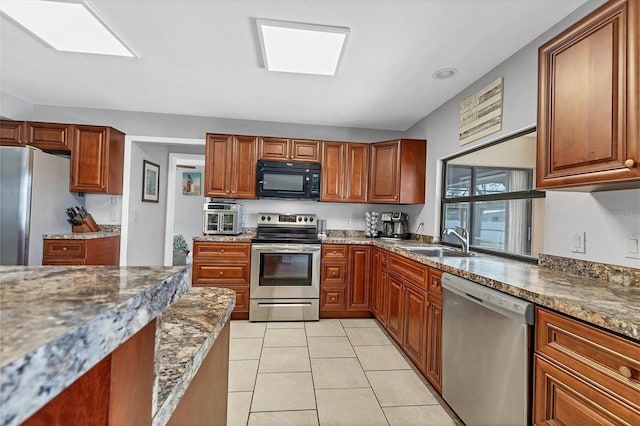 kitchen featuring light tile patterned floors, dark stone counters, a sink, appliances with stainless steel finishes, and brown cabinets