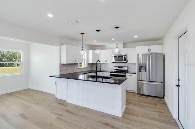 kitchen with appliances with stainless steel finishes, pendant lighting, sink, white cabinets, and backsplash