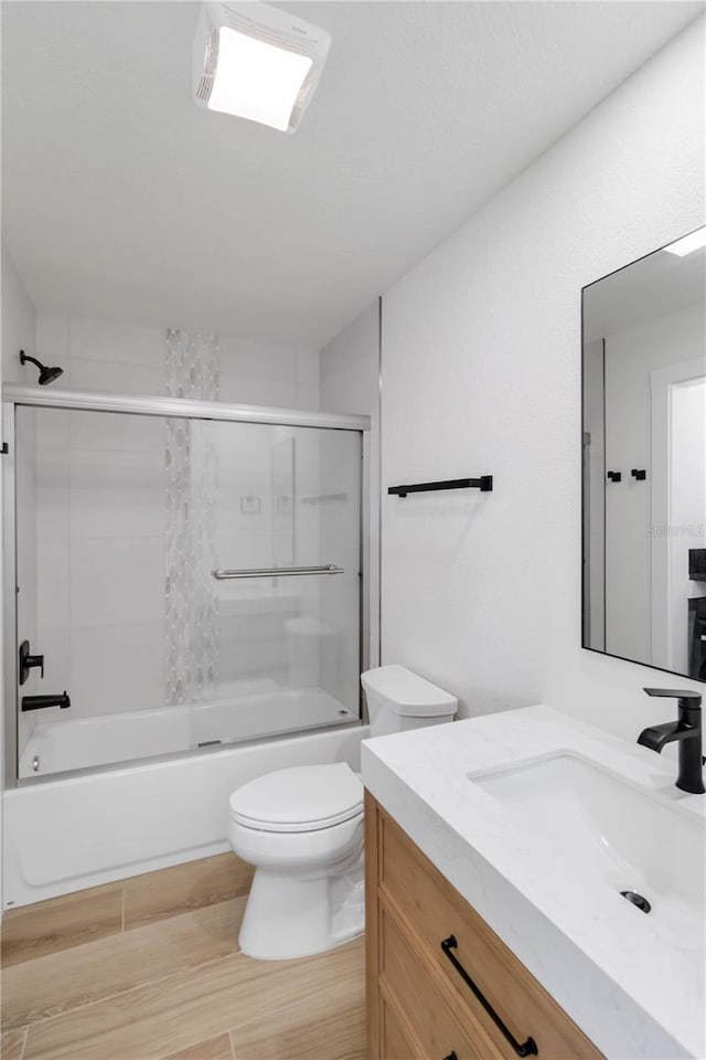 full bathroom featuring vanity, hardwood / wood-style floors, combined bath / shower with glass door, and toilet