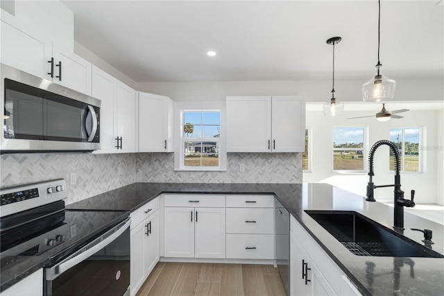 kitchen featuring appliances with stainless steel finishes, decorative light fixtures, tasteful backsplash, white cabinetry, and sink