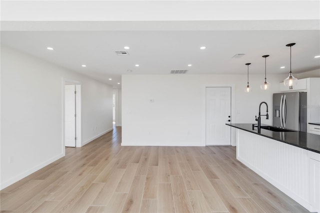 kitchen with sink, white cabinetry, light wood-type flooring, stainless steel fridge, and pendant lighting